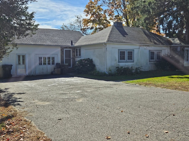 exterior space featuring aphalt driveway, a yard, roof with shingles, and a chimney