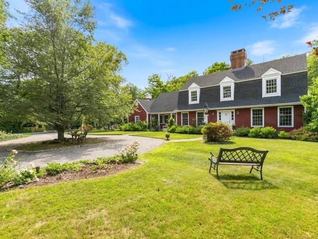 colonial inspired home with a chimney, driveway, roof with shingles, and a front yard