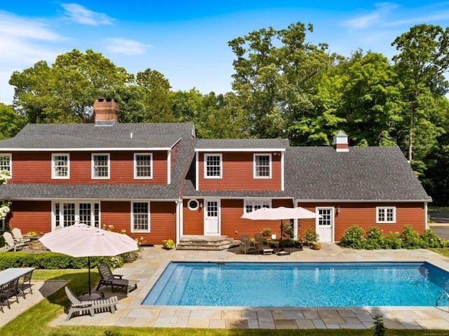 back of property featuring an outdoor pool, a shingled roof, a chimney, and a patio area