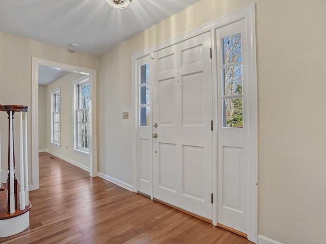 entryway with baseboards, a textured ceiling, and light wood-style flooring