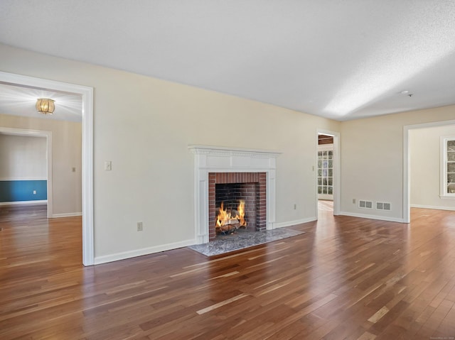 unfurnished living room featuring a brick fireplace, visible vents, baseboards, and wood-type flooring