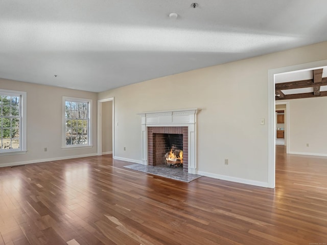 unfurnished living room featuring wood finished floors, a brick fireplace, baseboards, and beam ceiling