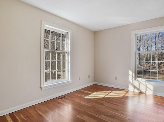 empty room featuring visible vents, baseboards, and hardwood / wood-style flooring