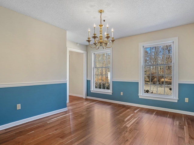 unfurnished room featuring hardwood / wood-style floors, a notable chandelier, baseboards, and a textured ceiling