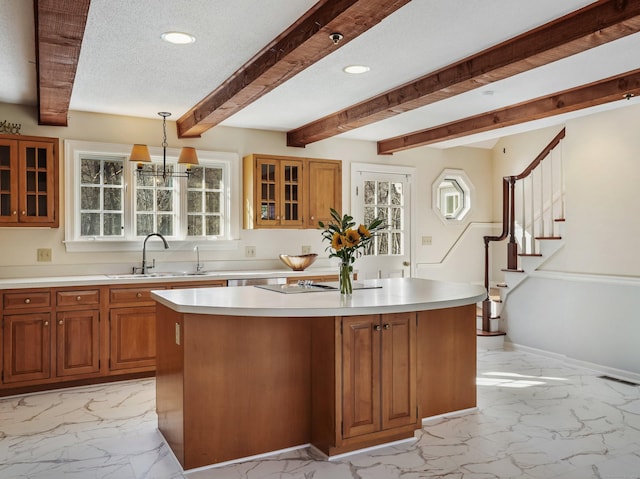 kitchen featuring marble finish floor, a sink, a center island, brown cabinetry, and light countertops