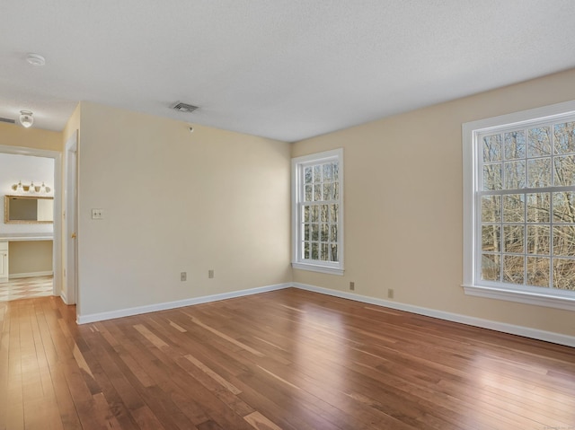 empty room featuring visible vents, a textured ceiling, baseboards, and wood-type flooring