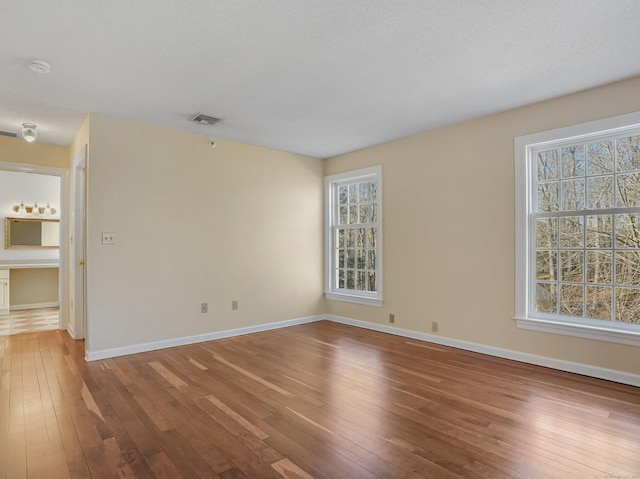 unfurnished room featuring baseboards, hardwood / wood-style floors, and visible vents