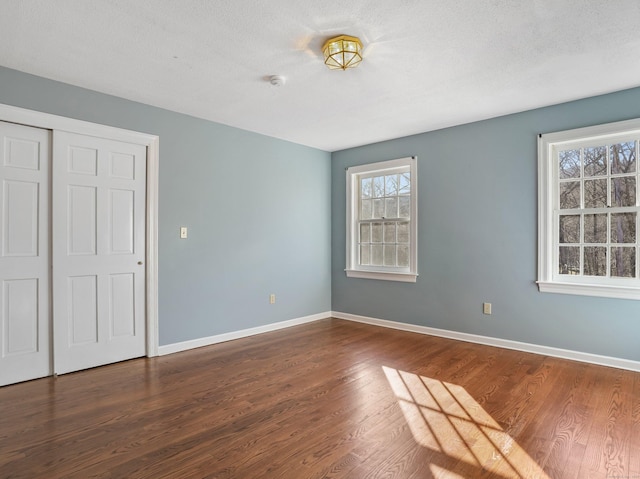 unfurnished bedroom featuring dark wood-style floors, a closet, and baseboards