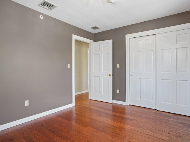 unfurnished bedroom featuring visible vents, baseboards, a closet, and wood finished floors