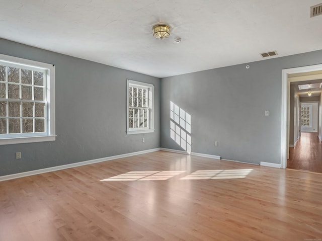 empty room with wood finished floors, visible vents, and baseboards