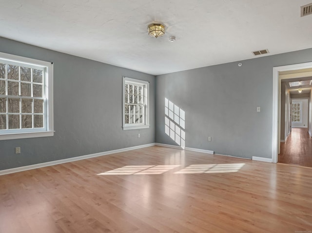 unfurnished room with a wealth of natural light, wood finished floors, and visible vents
