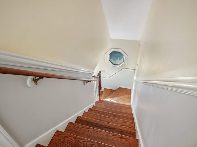 staircase featuring wood finished floors, lofted ceiling, and baseboards