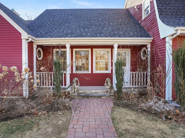 view of exterior entry featuring a porch and a shingled roof