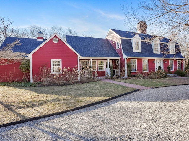 view of front of house featuring a gambrel roof, a front lawn, covered porch, a shingled roof, and a chimney