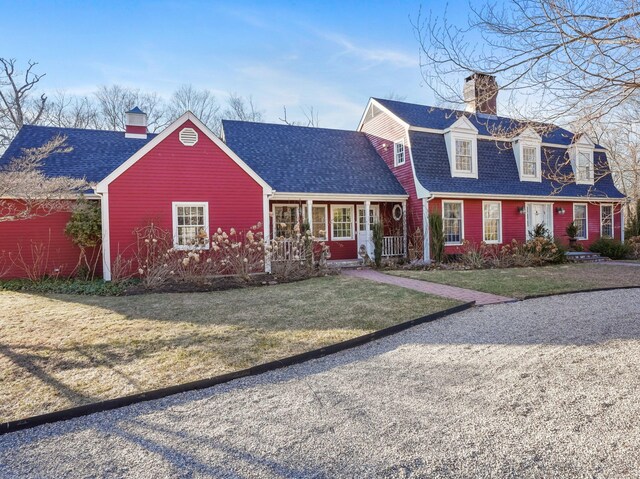 view of front of home featuring a front lawn, a chimney, covered porch, and roof with shingles