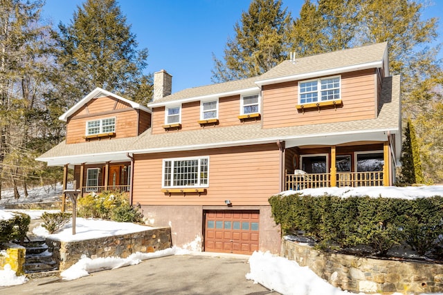 view of front of house featuring a shingled roof, covered porch, a chimney, and an attached garage