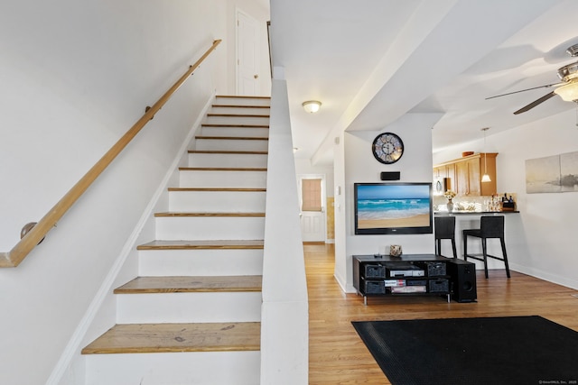 stairway with ceiling fan, wood finished floors, and baseboards