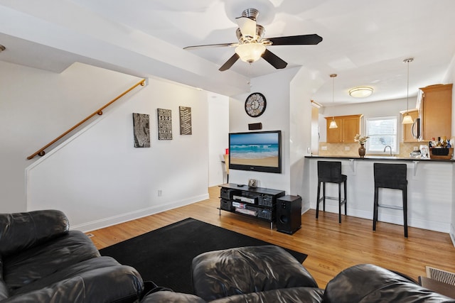 living room featuring visible vents, baseboards, ceiling fan, stairway, and light wood-type flooring