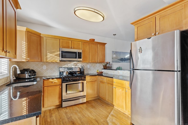 kitchen with light wood-style flooring, decorative backsplash, appliances with stainless steel finishes, a sink, and dark stone counters