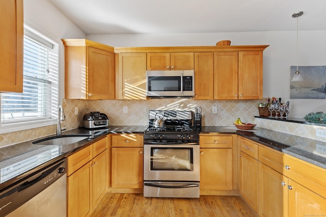 kitchen featuring light wood-style flooring, a sink, hanging light fixtures, appliances with stainless steel finishes, and dark stone counters