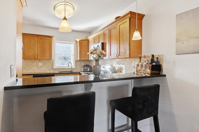 kitchen with dark countertops, hanging light fixtures, a sink, a peninsula, and a kitchen bar