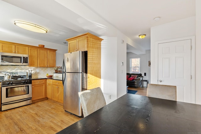 kitchen with dark countertops, light wood finished floors, stainless steel appliances, and backsplash