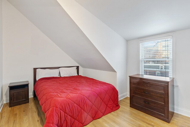 bedroom featuring lofted ceiling, baseboards, and light wood finished floors