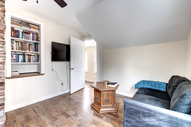 living area with a ceiling fan, wood finished floors, built in features, and baseboards