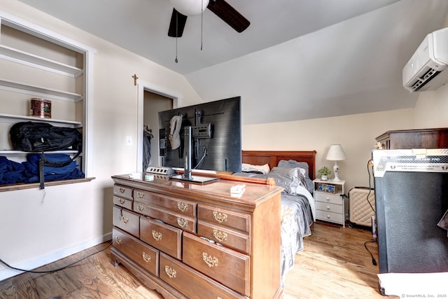 bedroom with lofted ceiling, light wood-style flooring, baseboards, and a wall mounted air conditioner