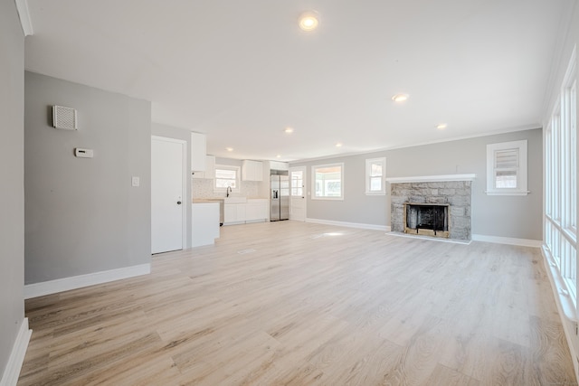 unfurnished living room featuring recessed lighting, baseboards, a stone fireplace, and light wood finished floors