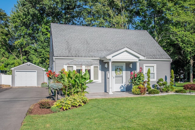 new england style home with roof with shingles, a front yard, a garage, driveway, and an outdoor structure