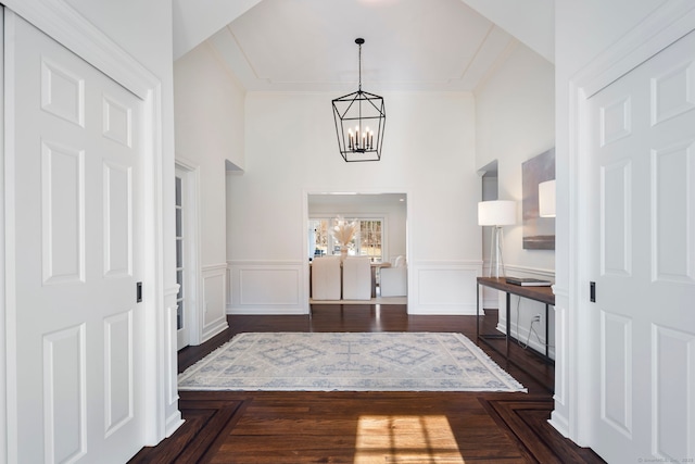 entryway featuring dark wood-style floors, a chandelier, wainscoting, and a decorative wall