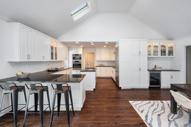 kitchen featuring glass insert cabinets, dark countertops, beverage cooler, and a peninsula