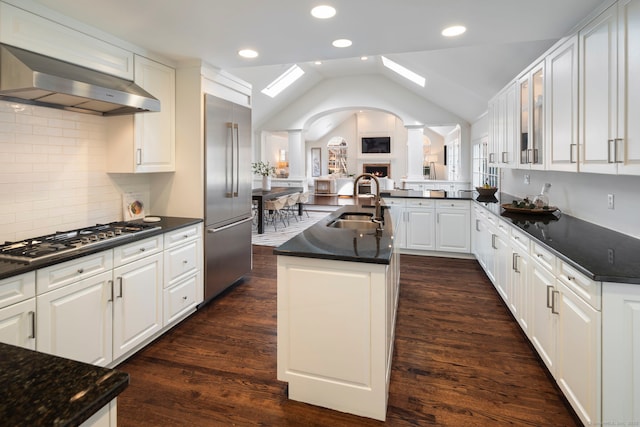 kitchen featuring lofted ceiling, stainless steel appliances, a sink, range hood, and ornate columns