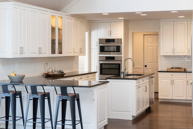 kitchen featuring a peninsula, white cabinetry, appliances with stainless steel finishes, decorative backsplash, and dark countertops