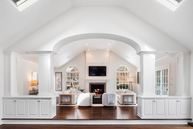 living room with vaulted ceiling with skylight, a fireplace, decorative columns, and wood finished floors