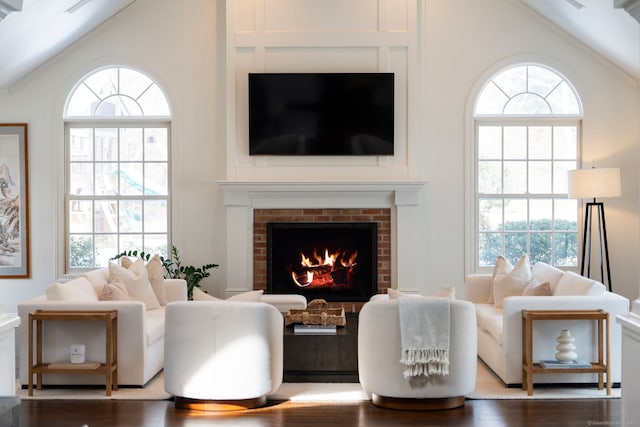 living area featuring lofted ceiling, a brick fireplace, wood finished floors, and a wealth of natural light