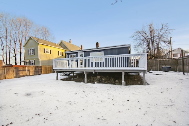 snow covered back of property with a deck and a fenced backyard