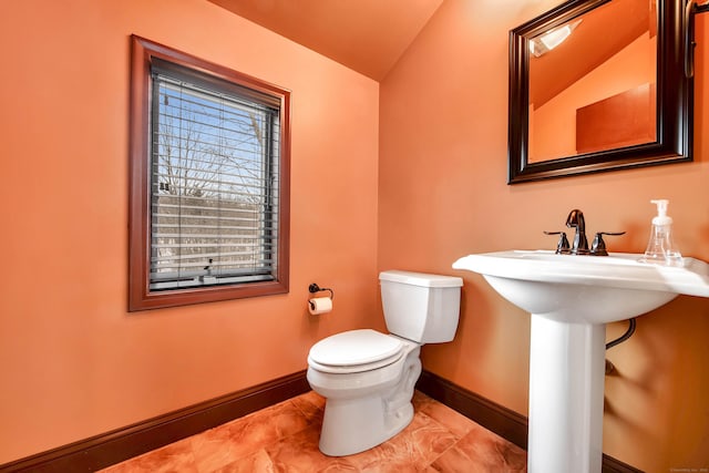 half bathroom featuring vaulted ceiling, a sink, toilet, and baseboards