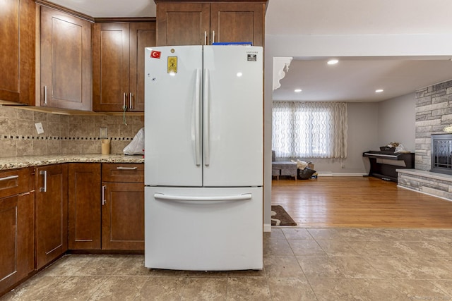 kitchen with a fireplace, light hardwood / wood-style flooring, light stone countertops, backsplash, and white fridge