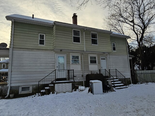 snow covered back of property with a chimney and fence