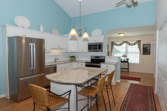 kitchen with decorative light fixtures, appliances with stainless steel finishes, white cabinets, a kitchen island, and a sink