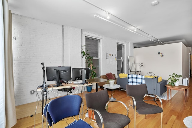 office space featuring brick wall, light wood-style flooring, and rail lighting