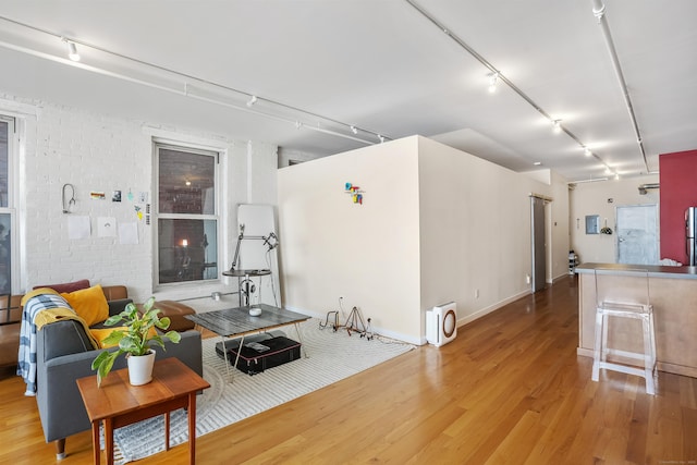 living area featuring light wood-type flooring, rail lighting, and brick wall