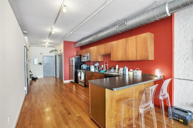 kitchen featuring brown cabinetry, a peninsula, rail lighting, stainless steel appliances, and light wood-style floors