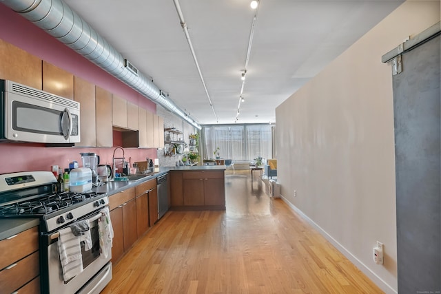 kitchen with light wood finished floors, stainless steel appliances, dark countertops, rail lighting, and a sink