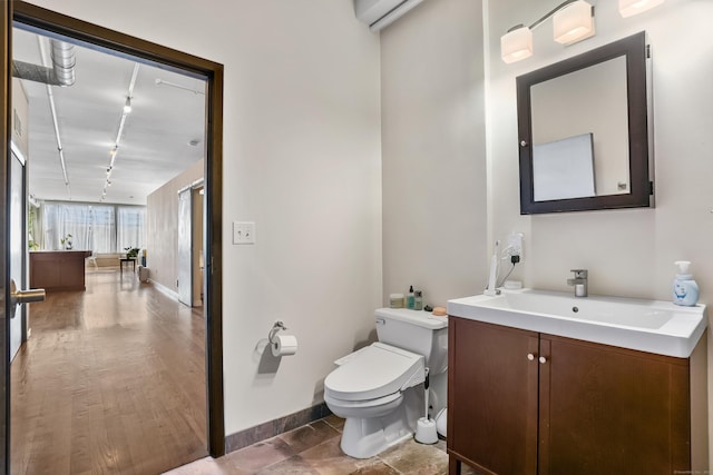 half bath with toilet, vanity, rail lighting, and baseboards