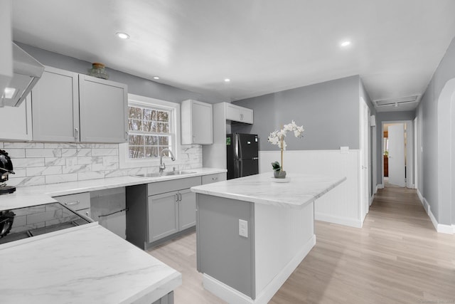 kitchen with light wood-style flooring, a sink, a center island, freestanding refrigerator, and decorative backsplash