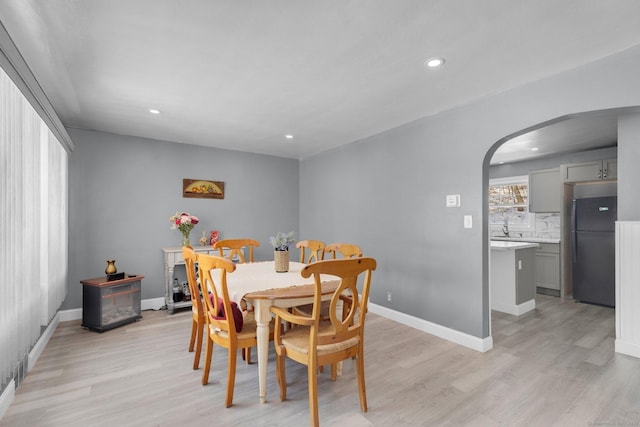 dining space featuring arched walkways, recessed lighting, light wood-style flooring, and baseboards