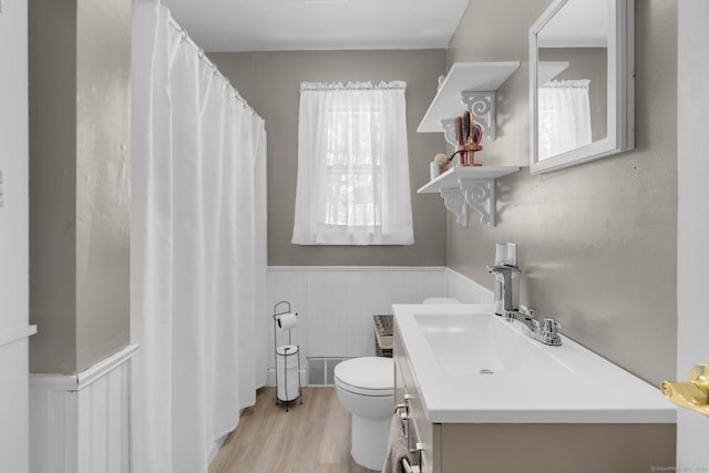 bathroom with a wainscoted wall, visible vents, toilet, vanity, and wood finished floors